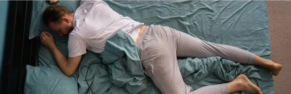 man in white tee shirt and sweatpants, sleeping soundly on his stomach with teal blue bedsheets